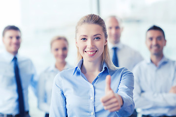 Image showing smiling businesswoman showing thumbs up in office