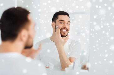 Image showing happy young man applying cream to face at bathroom