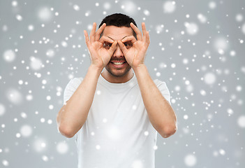 Image showing man making finger glasses over snow background