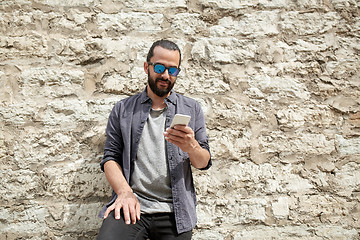 Image showing man texting message on smartphone at stone wall