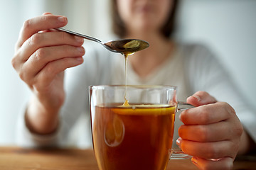 Image showing close up of woman adding honey to tea with lemon