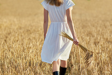 Image showing young woman with cereal spikelets walking on field