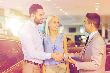 Image showing happy couple with car dealer in auto show or salon