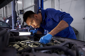Image showing mechanic man with lamp repairing car at workshop