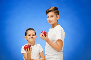 Image showing Handsome little boys with two red apples. Studio portrait over blue background