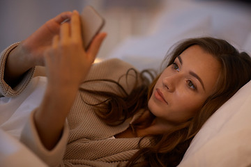 Image showing young woman with smartphone in bed at home bedroom