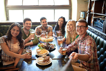 Image showing happy friends with selfie stick at bar or pub