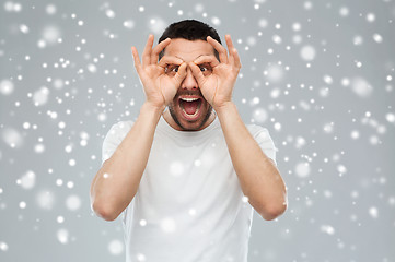 Image showing man making finger glasses over snow background