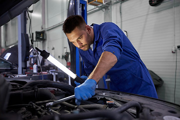 Image showing mechanic man with lamp repairing car at workshop