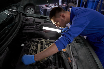 Image showing mechanic man with lamp repairing car at workshop