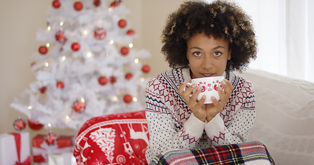 Image showing Pretty woman sipping from cup while seated on sofa