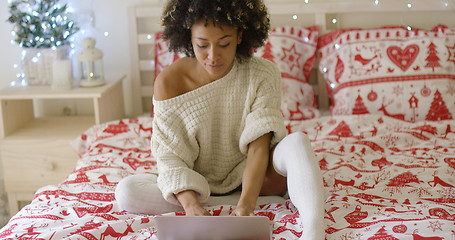 Image showing Woman in oversized sweater on bed using laptop