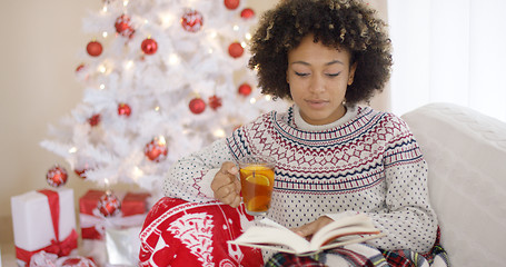 Image showing Woman reading a book in front of Christmas tree