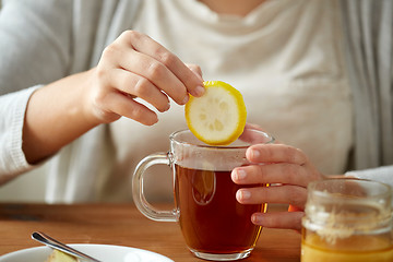 Image showing close up of woman adding lemon to tea with honey