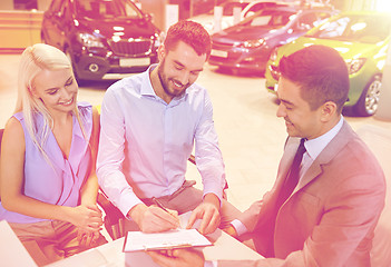 Image showing happy couple with car dealer in auto show or salon