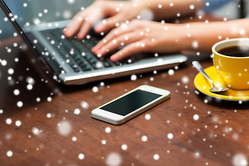 Image showing close up of smartphone and hands typing on laptop