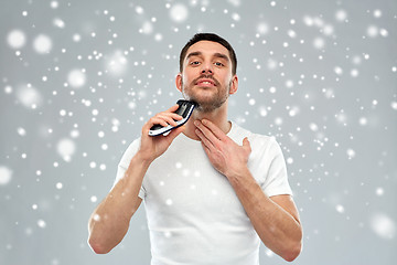 Image showing smiling man shaving beard with trimmer over snow