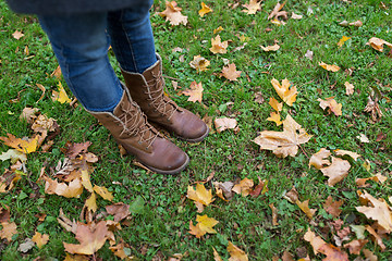 Image showing female feet in boots and autumn leaves on grass