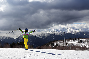 Image showing Happy young skier with ski poles in sun mountains and cloudy gra