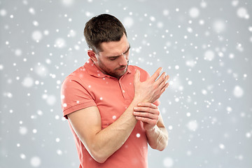 Image showing unhappy man suffering from pain in hand over snow