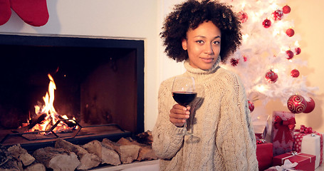 Image showing Pretty woman holds wine glass beside fireplace