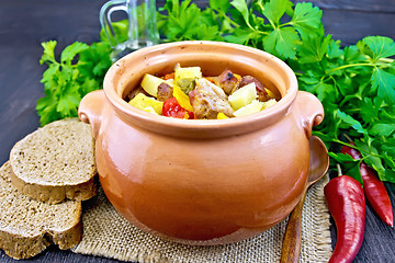 Image showing Roast meat and vegetables in clay pot on dark board