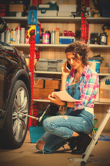 Image showing car mechanic woman in blue overalls talking on the phone near a 