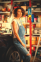 Image showing curly-haired woman in blue overalls mechanic near a car 