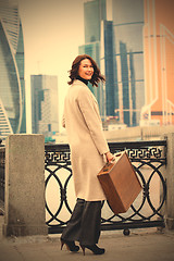 Image showing smiling woman in a bright coat with wooden case in her hand