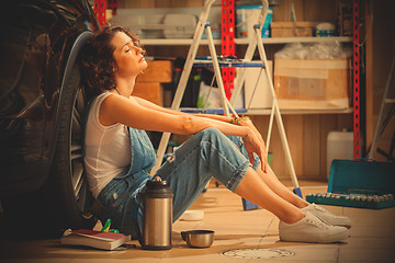 Image showing auto mechanic woman in blue overalls resting near the wheel of t