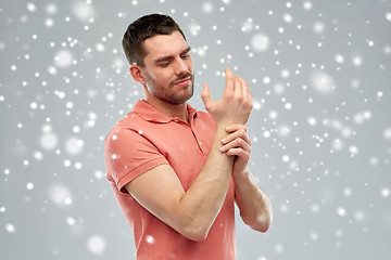 Image showing unhappy man suffering from pain in hand over snow