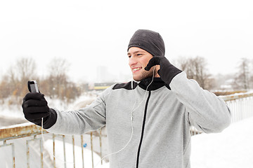 Image showing happy man with earphones and smartphone in winter