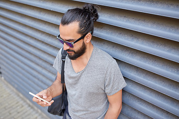 Image showing man with bag texting on smartphone in city