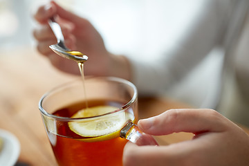 Image showing close up of woman adding honey to tea with lemon