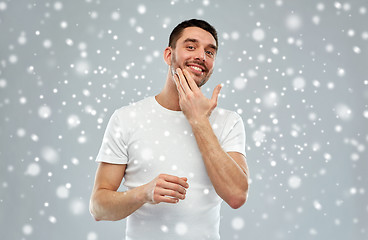 Image showing happy young man applying cream or lotion to face