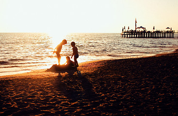 Image showing lifestyle people concept: three little boys silhouette on sunset beach playing in water