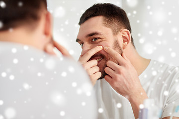 Image showing smiling man squeezing pimple at bathroom mirror