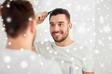 Image showing happy man brushing hair with comb at bathroom