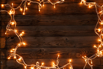 Image showing Dark brown wooden background with shining garland on the frame