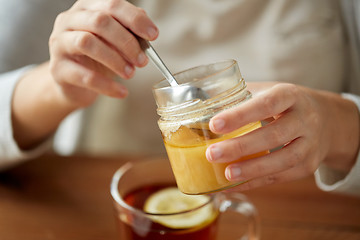 Image showing close up of woman adding honey to tea with lemon