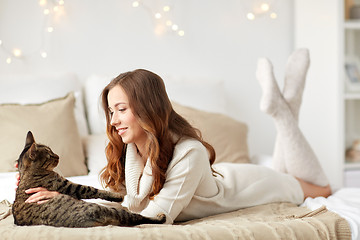 Image showing happy young woman with cat lying in bed at home