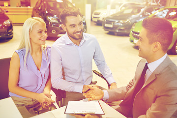 Image showing happy couple with car dealer in auto show or salon