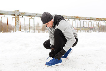 Image showing man with earphones tying sports shoes in winter