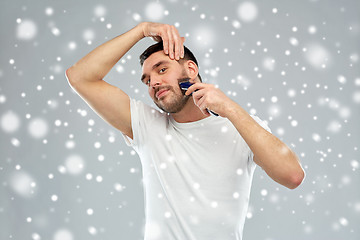 Image showing smiling man shaving beard with trimmer over snow