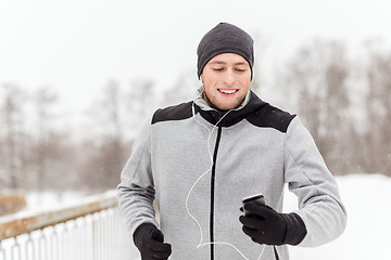 Image showing happy man with earphones and smartphone in winter