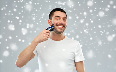 Image showing smiling man shaving beard with trimmer over snow