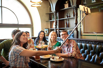 Image showing happy friends with selfie stick at bar or pub
