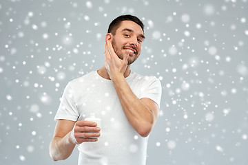 Image showing happy young man applying cream or lotion to face