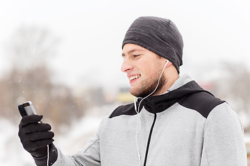 Image showing happy man with earphones and smartphone in winter