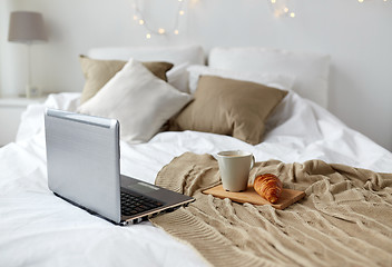 Image showing laptop, coffee and croissant on bed at cozy home